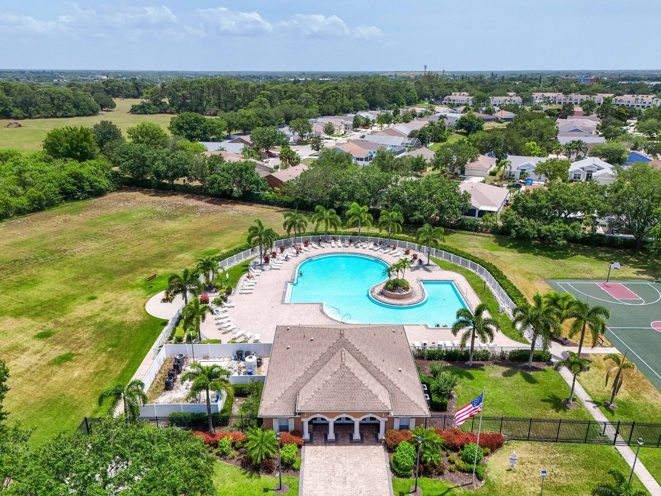 An aerial view of a resort with a large swimming pool, a tennis court, and a building with a tiled roof.