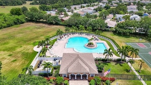 An aerial view of a resort with a large swimming pool, a tennis court, and a building with a tiled roof.