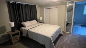A bedroom with a bed, a nightstand, a lamp, a closet, and a door leading to another room. - Cozy 3BR home close to trails. (Logan)