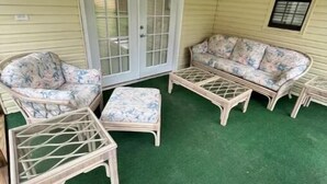 A covered patio area with a ceiling fan, two wicker sofas with floral cushions, a small table, and a glass door. - Cozy 3BR home close to trails. (Logan)