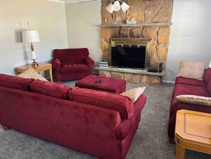 A living room with a stone fireplace, red sofas, a television, and a lamp.