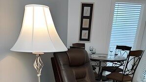 Et moderne værelse med en læderstol, et rundt bord med lampe og et spiseområde i baggrunden.