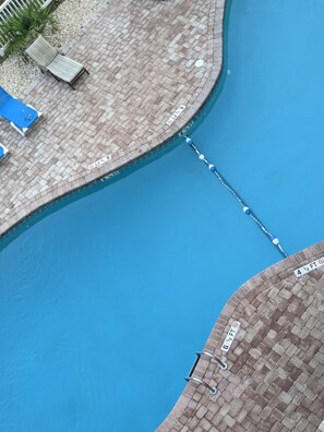 Piscina com trampolim, cadeiras de descanso e um terraço de tijolos.