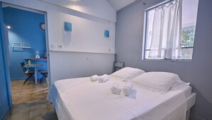 Un dormitorio con una cama, dos mesitas de noche, una ventana con cortinas, un escritorio con una silla y una pared azul con un reloj.
