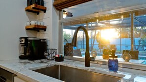 Eine Küche mit Spüle, einer Kaffeemaschine und einem Fenster mit Blick auf einen Garten.