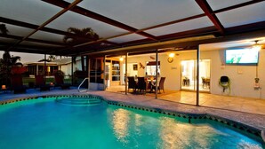 Ein Swimmingpool mit überdachter Terrasse, Essbereich und Fernseher.