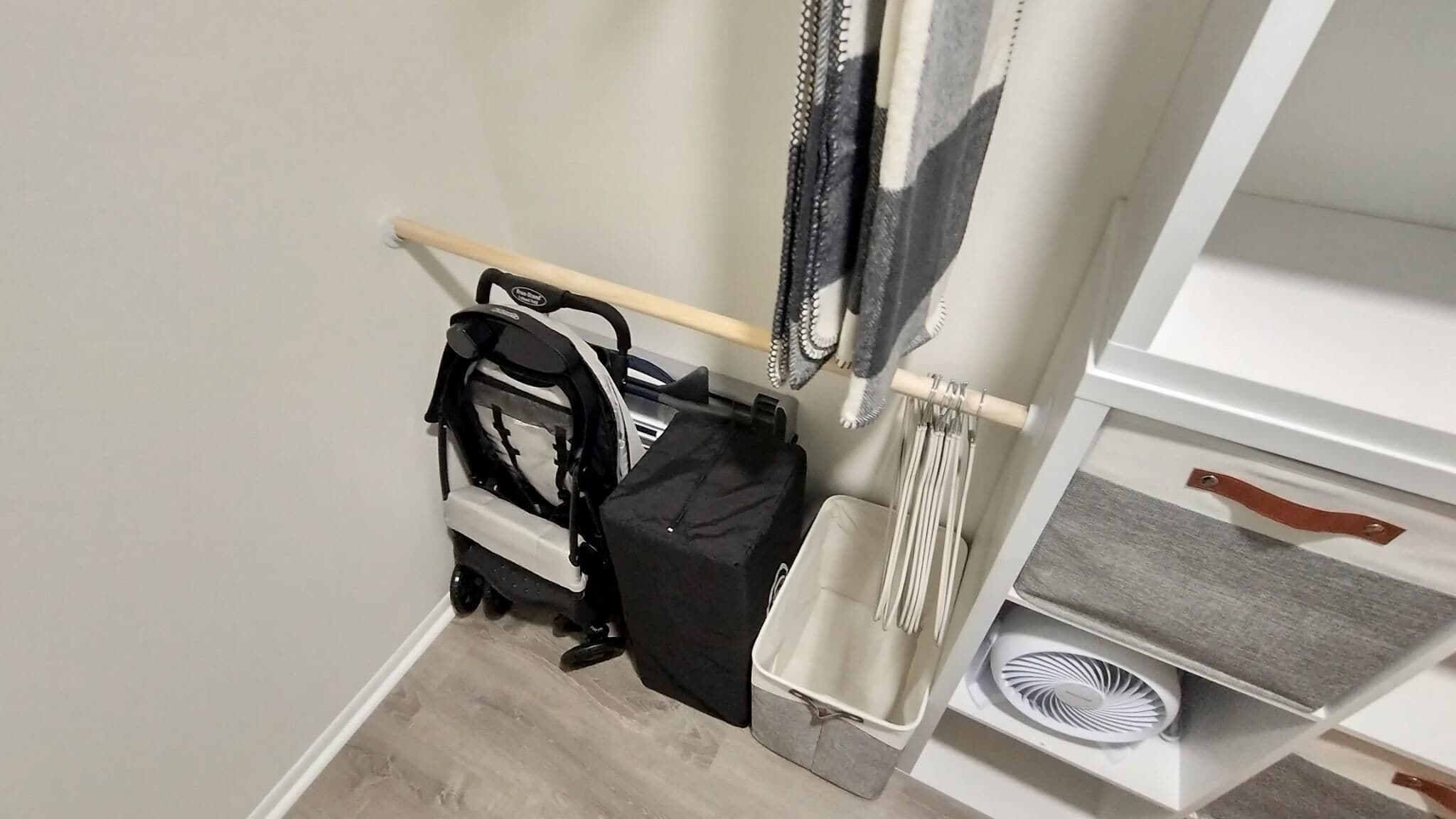 Un coin de pièce avec une poussette, un petit panier blanc et une étagère sur laquelle se trouve un ventilateur.