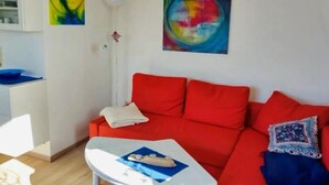 Ett vardagsrum med en röd soffa, ett vitt soffbord och två abstrakta tavlor på väggen.