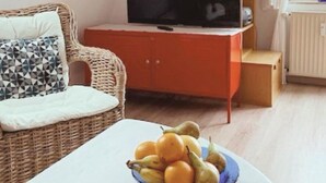 Ett vardagsrum med en soffa av rotting, en tv på ett rött skåp och en fruktskål på ett bord.