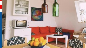 Ett modernt vardagsrum med en röd soffa, ett matbord med en fruktskål, ett vitt skåp med porslin och en färgstark, abstrakt målning.
