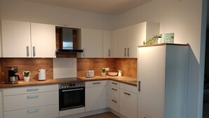 Una cocina moderna con armarios blancos, horno empotrado, cafetera y una pequeña planta en maceta.
