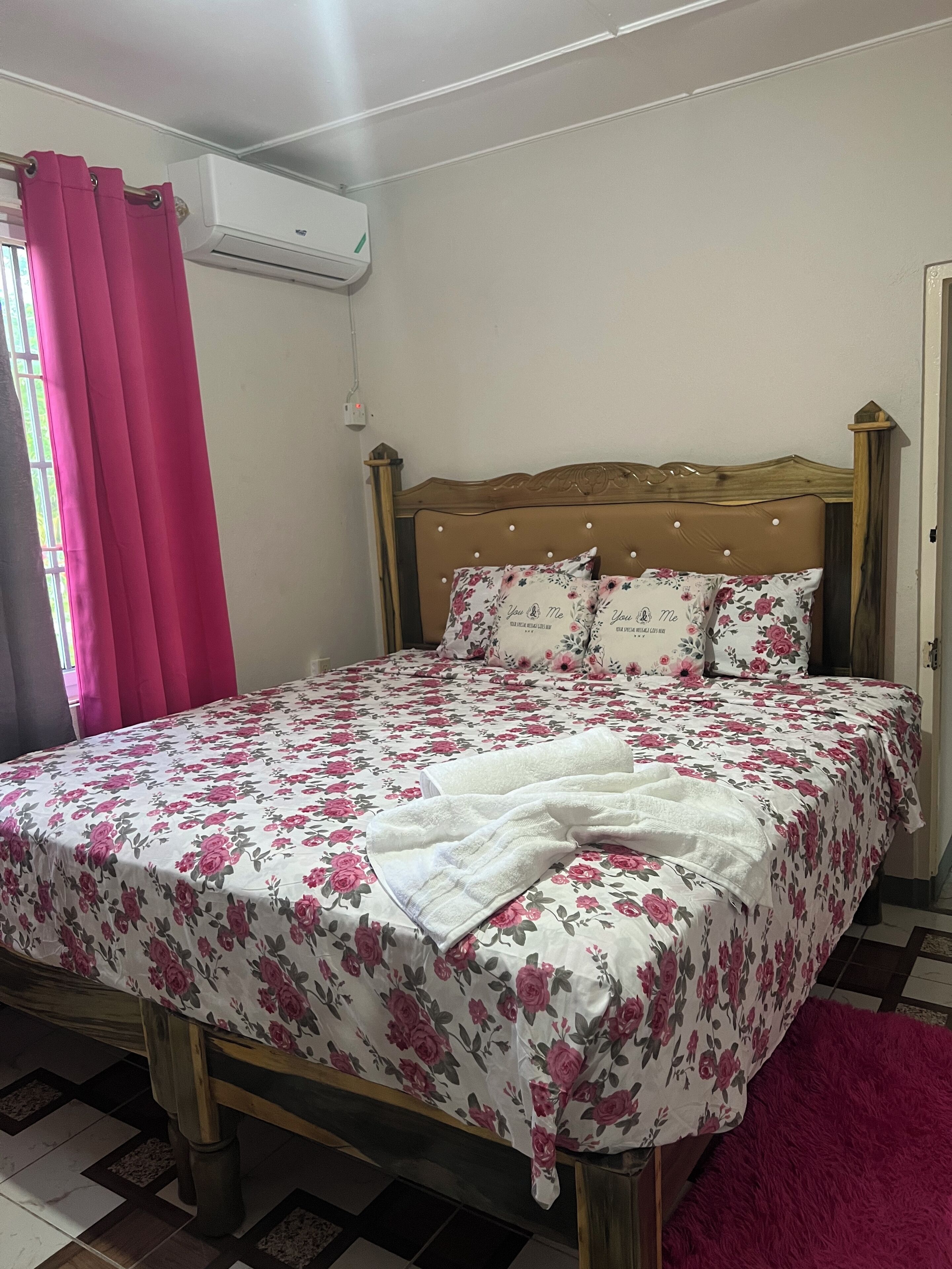 A bedroom with a floral bedspread, a wooden headboard, and a pink curtain.