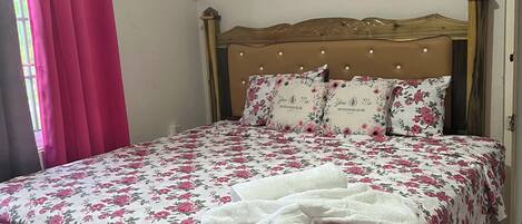 A bedroom with a floral bedspread, a wooden headboard, and a pink curtain.