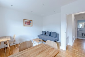 A modern living room with a grey sofa, wooden coffee table, and a dining table with chairs.