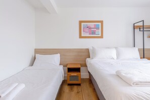 A hotel room with two single beds, a wooden headboard, a small wooden nightstand, and a framed abstract painting on the wall.