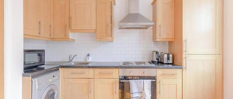 A compact kitchen with wooden cabinets, a built-in oven, a microwave, and a washing machine.