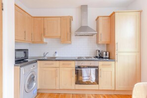 Une cuisine compacte avec des meubles en bois, un four encastré, un four à micro-ondes et un lave-linge.