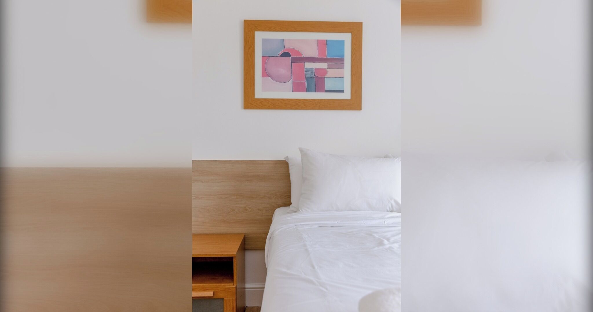Een hotelkamer met een houten hoofdeinde, een wit bed en een klein nachtkastje.