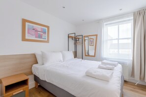 A hotel room with a bed, a bedside table, a window with curtains, and artwork on the wall.