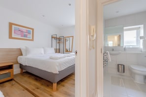 A modern hotel room with a bed, bedside table, and a bathroom with a sink and toilet.