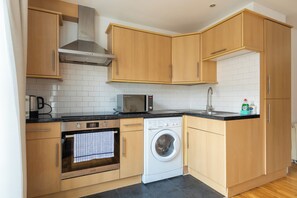 A modern kitchen with wooden cabinets, a microwave, an oven, a washing machine, and a sink. - Spacious and Newly Renovated 2BD Flat Camden Town (London)
