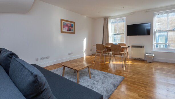 Una sala de estar moderna con un sofá, una mesa de comedor con sillas, un televisor de pantalla plana montado en la pared y un radiador.