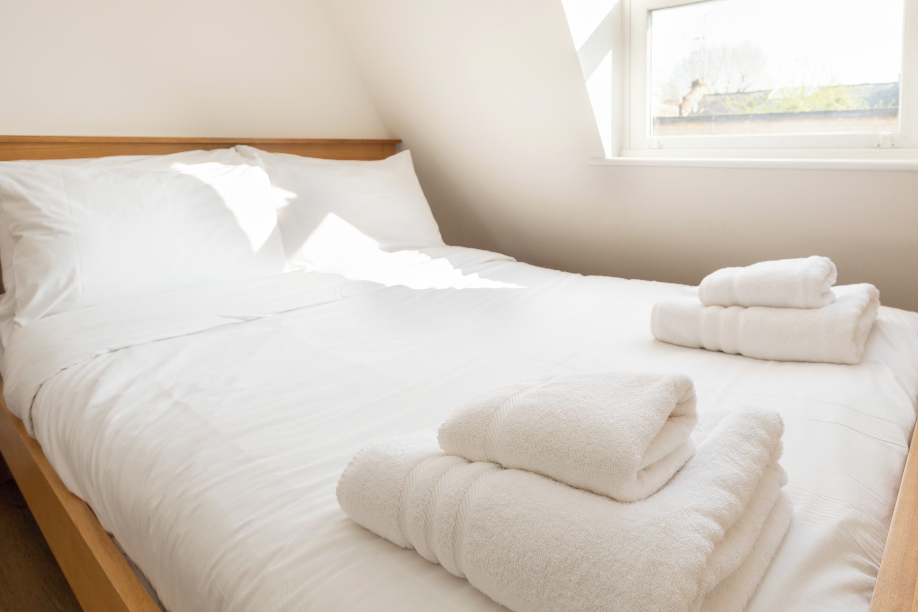 A neatly made bed with white linens and two folded towels on the side.