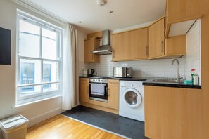 Une cuisine moderne avec des meubles en bois, une hotte de cuisine en acier inoxydable, un four encastré, un lave-linge et une fenêtre avec des rideaux.
