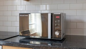 Un horno microondas de acero inoxidable con pantalla digital, sobre una encimera negra con salpicadero de azulejos blancos.