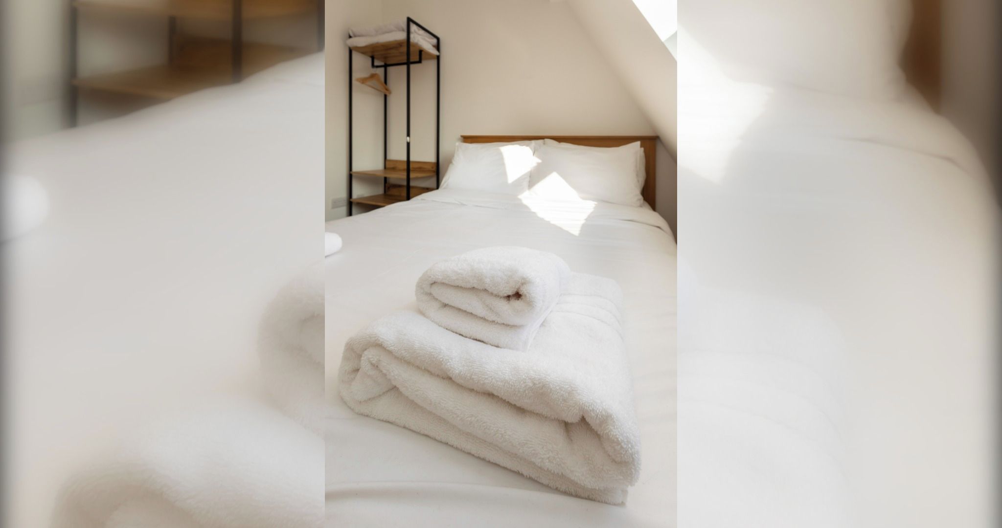 Cama bem arrumada com toalha branca dobrada em quarto com cabeceira de madeira e suporte metálico.