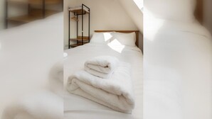 A neatly made bed with a folded white towel in a room with a wooden headboard and a metal rack. - Spacious and Newly Renovated 2BD Flat Camden Town (London)