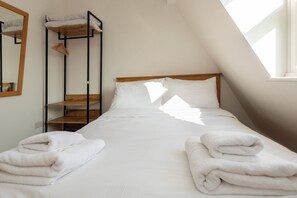 A neatly made bed with white linens and towels, a wooden headboard, and a bunk bed with a mirror and clothes rack. - Spacious and Newly Renovated 2BD Flat Camden Town (London)