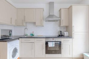 Une cuisine moderne avec des meubles blancs, un four en acier inoxydable, un lave-linge et un four à micro-ondes.