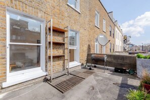 A brick building with a large window, a metal ladder, and a satellite dish. - Bright Urban Retreat Balcony Camden (London)
