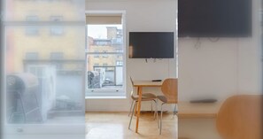 Ein Zimmer mit Fenster, einem Tisch, zwei Stühlen und einem an der Wand befestigten Flachbildfernseher.