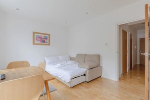 A bedroom with a bed, a desk, and a chair. There is a door leading to another room.
