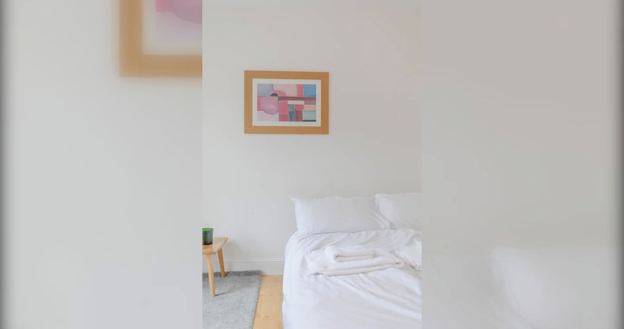 Una habitación de hotel con cama, una mesita y un cuadro enmarcado en la pared.