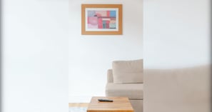 Un salón minimalista con un sofá beige, una mesa de centro de madera y un cuadro abstracto enmarcado en la pared.