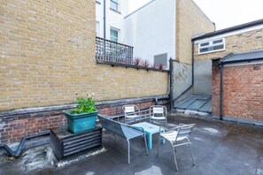 Eine Dachterrasse mit einem Metalltisch und -stühlen, einem Blumentopf und einer Ziegelwand.