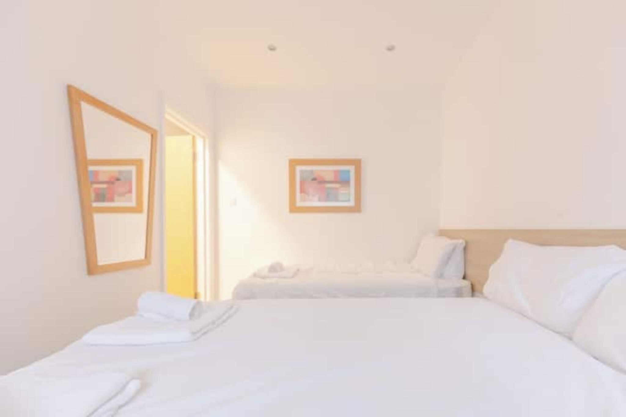 A hotel room with two beds, a large mirror, and a framed picture on the wall.