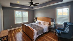 Ein Schlafzimmer mit einem hölzernen Bett, zwei Nachttischen mit Lampen, einem blauen Sessel und einem Deckenventilator.