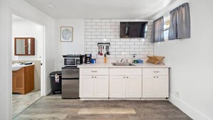 A modern kitchen with white cabinets, a microwave, a sink, and a television mounted above the counter. - Oceanview Studio Near Downtown & Cruise Terminal (Galveston)