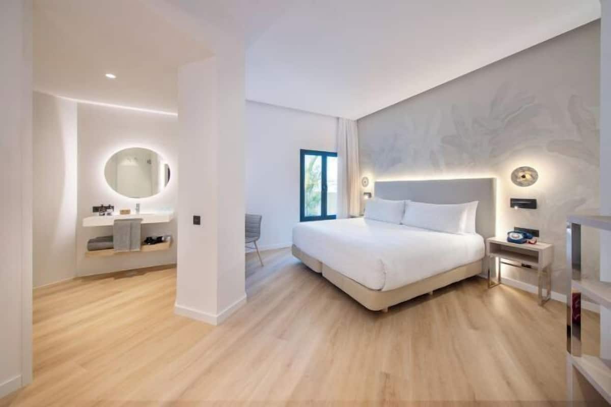 Ein modernes Schlafzimmer mit einem großen Bett, einem Nachttisch, einem Beistelltisch, einem runden Spiegel und einem Fenster.