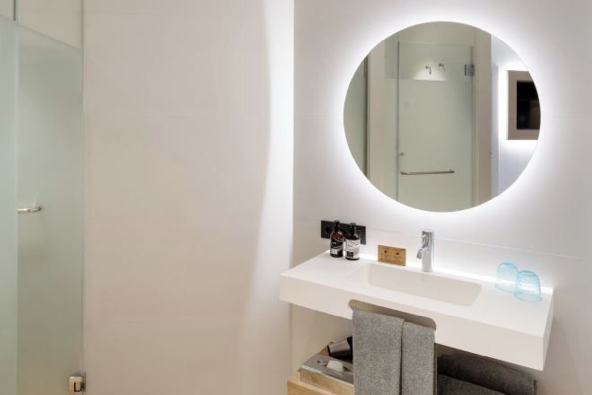 Un baño con tocador blanco, espejo redondo con luz y toallero.