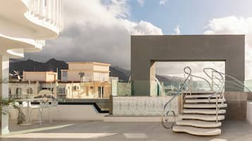 Un espacio exterior moderno con barandilla de vidrio, una escalera en espiral y vistas a montañas.