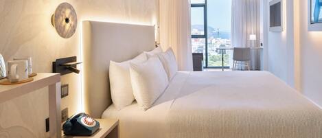 A modern hotel room with a large bed, a bedside table with a telephone, a view of the city through large windows, and a cityscape visible outside.