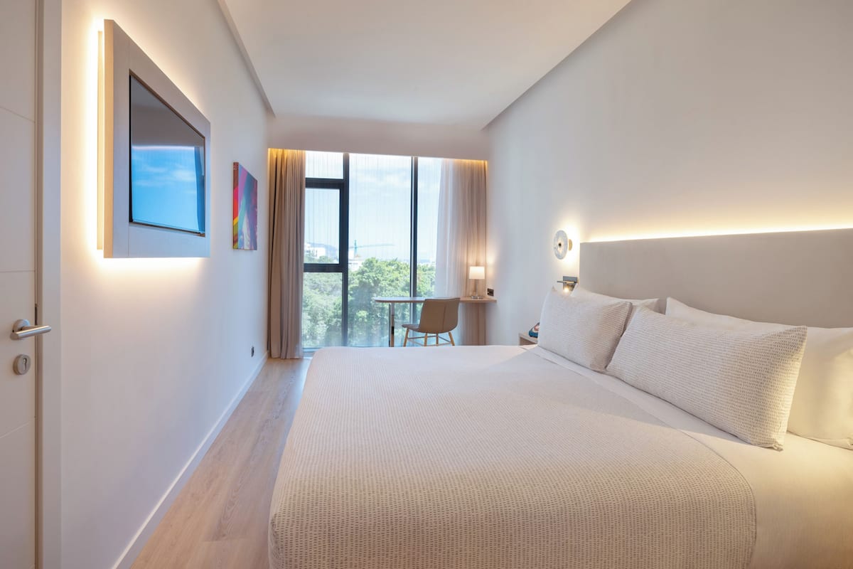Ein modernes Hotelzimmer mit einem großen Bett, einem Schreibtisch und Blick auf die Stadt durch das Fenster.