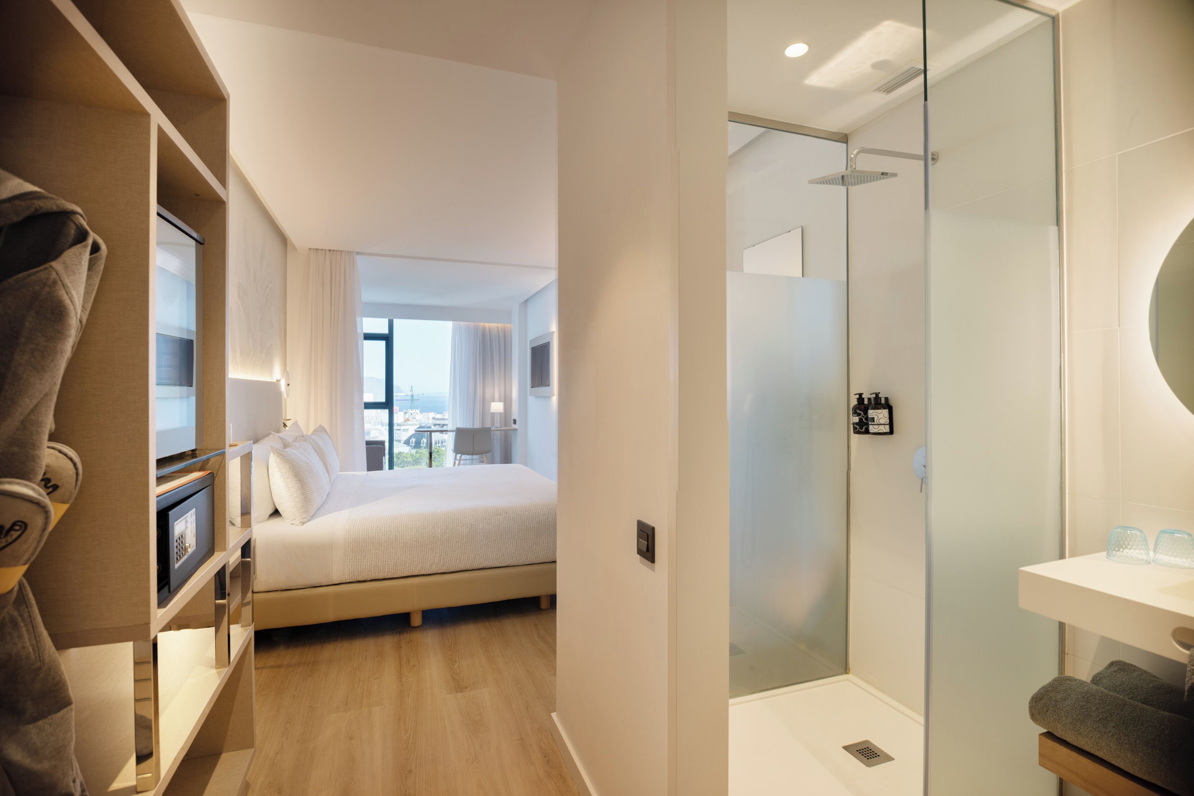 Habitación de hotel con cama, zona de ducha y vistas a la ciudad.
