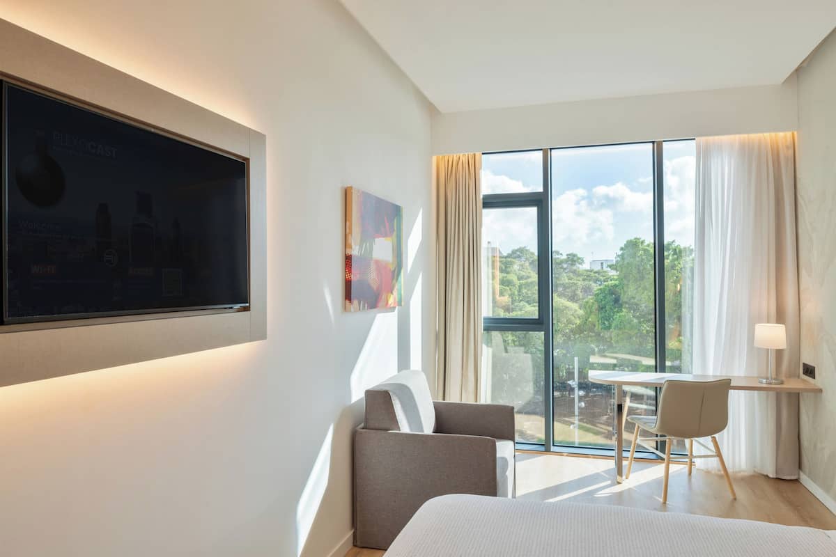 Ein modernes Hotelzimmer mit großem Fenster, Schreibtisch, Stuhl und Bett.