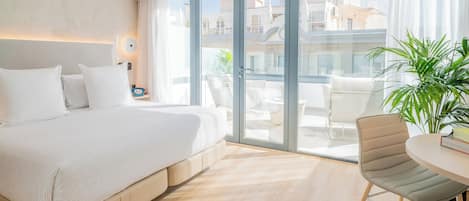 Quarto de hotel moderno com uma cama grande, uma varanda com vista para edifícios, uma mesa redonda e uma cadeira.